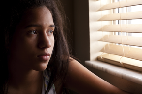Photo of a woman looking out of a window like she is sad.