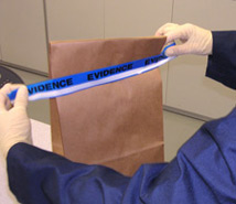 Photo of gloved hands holding up a brown paper evidence bag