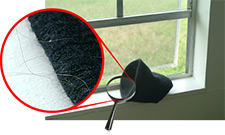 photo of a hat on a windowsill, a magnifying glass shows a closeup of hair on the hat. 