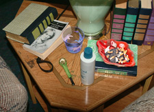 Photo of an end table with multiple items on it: books, drinking glass, ashtray, etc.