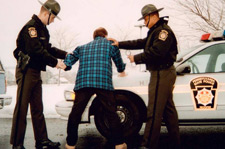 Photo of two police offices arresting a man in a plaid jacket