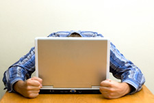Photo of a man with his head down, grabbing a laptop in desperation