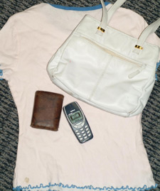 Photo of a woman's t shirt with a purse, wallet, and old 1990's cellphone on top