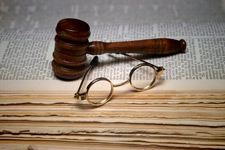Photo of a judge's gavel, and old timey glasses on top of a law book