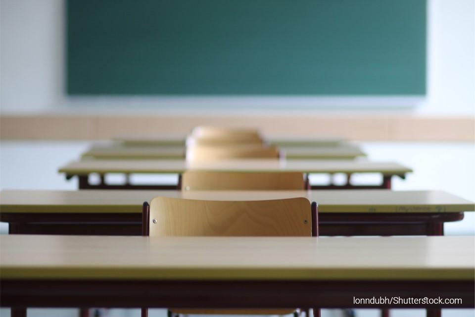 Stock image of several wooden school desks lined up facing the front of the classroom