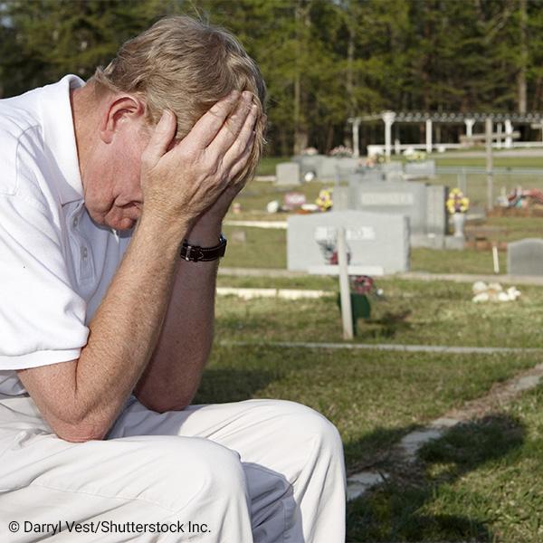 Older man sitting in cementary with hands over eyes
