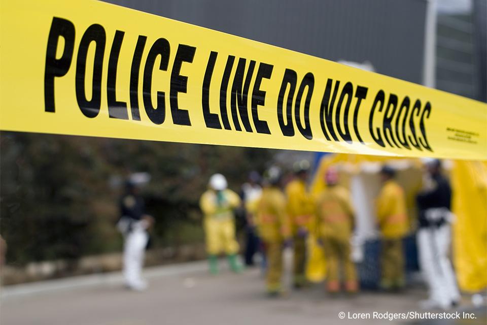 close-up of crime scene tape with first responders in background