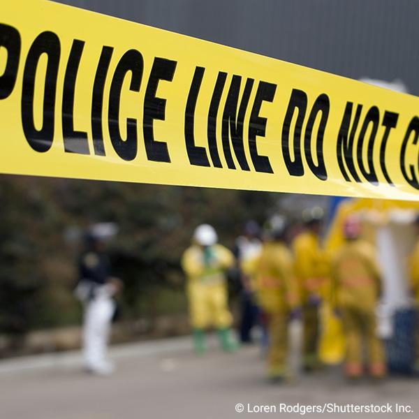 close-up of crime scene tape with first responders in background