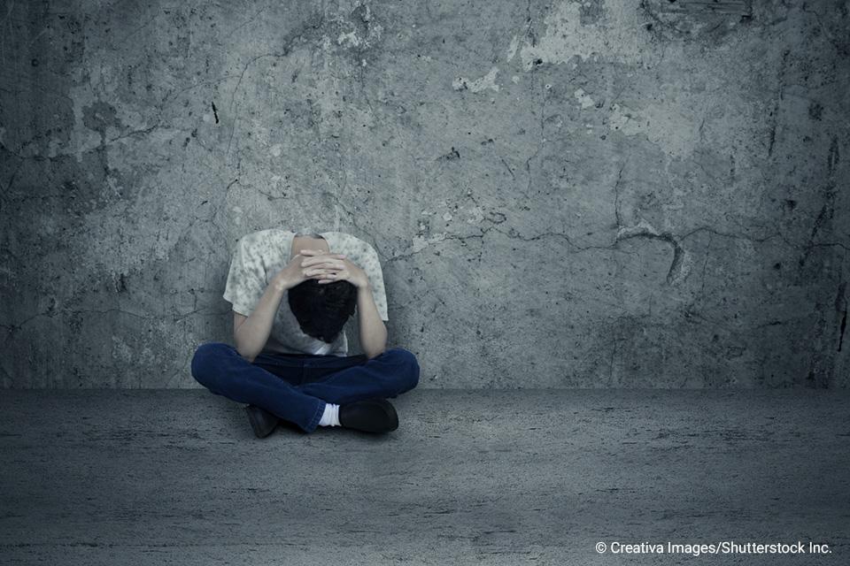 person sitting cross-legged with head down and hands over head