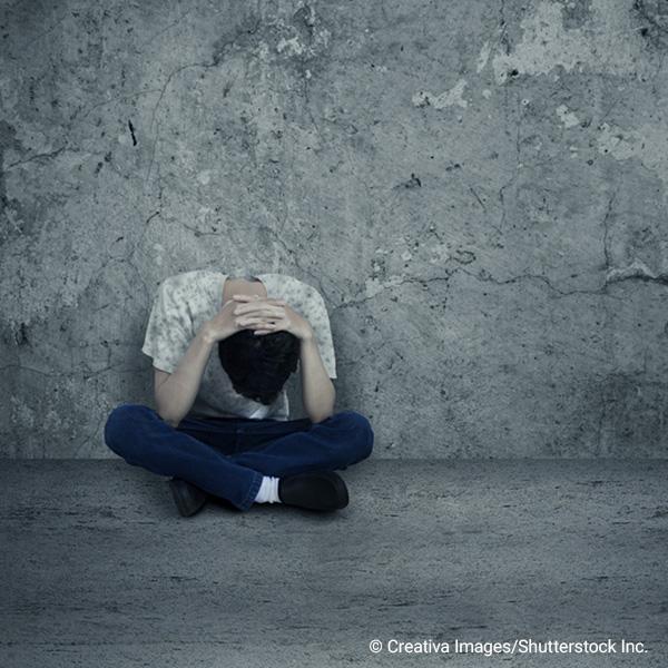 person sitting cross-legged with head down and hands over head