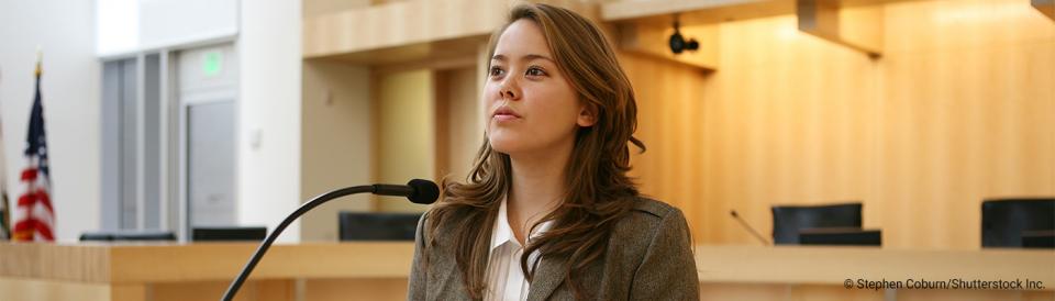 woman standing before a microphone in courtroom setting