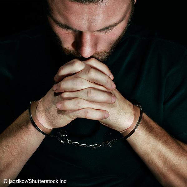 man in handcuffs looking down with face in hands