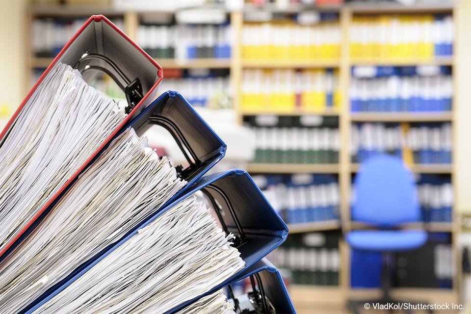 stacked binders with shelves of binders in background
