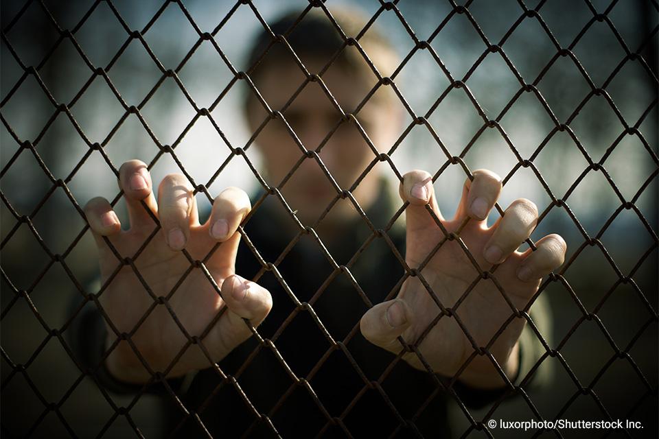 man behind a chain link fence with hands gripping fence