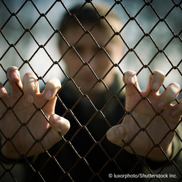 man behind a chain link fence with hands gripping fence