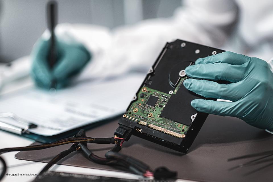 someone working in a lab wearing plastic gloves, taking notes about a digital device