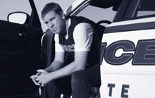 Officer sitting with legs outside open squad car door.